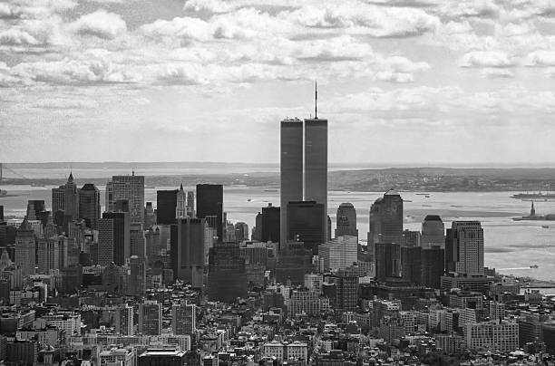 Historic black-and-white panoramic view of Lower Manhattan centered on the original World Trade Center Twin Towers, with New York Harbor, the Statue of Liberty and distant shoreline visible beyond the city skyline. (Credit: SteinPhoto)